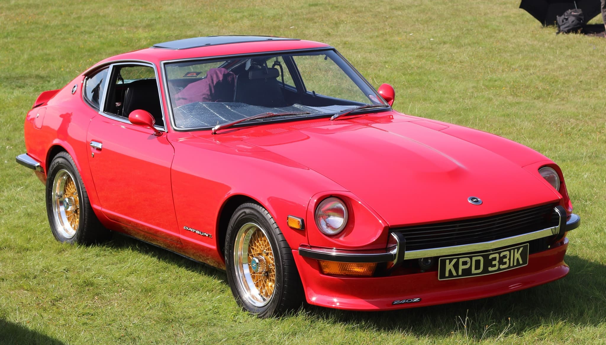 A red long-nosed fastback coupé with gold mesh alloy wheels on grass.