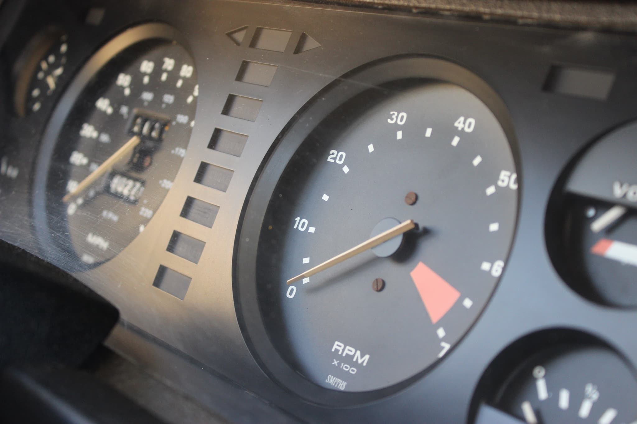 A close-up of a car's instrument binnacle, the rev counter in focus beside a strip of warning lamps. Opens a larger view