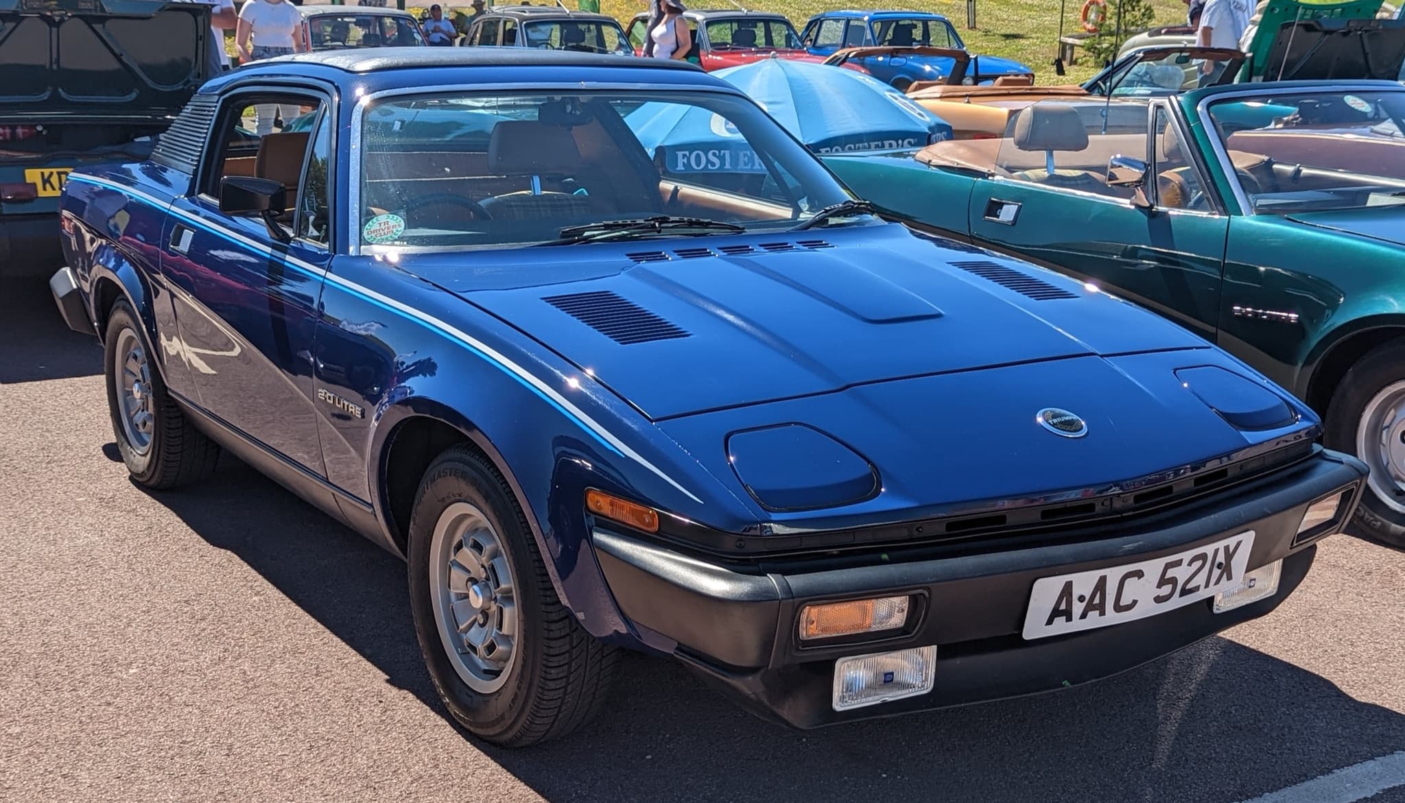 A dark blue coupé with a white coachline, a small round nose badge and a 2.0 Litre wing badge, in a car park. Opens a larger view