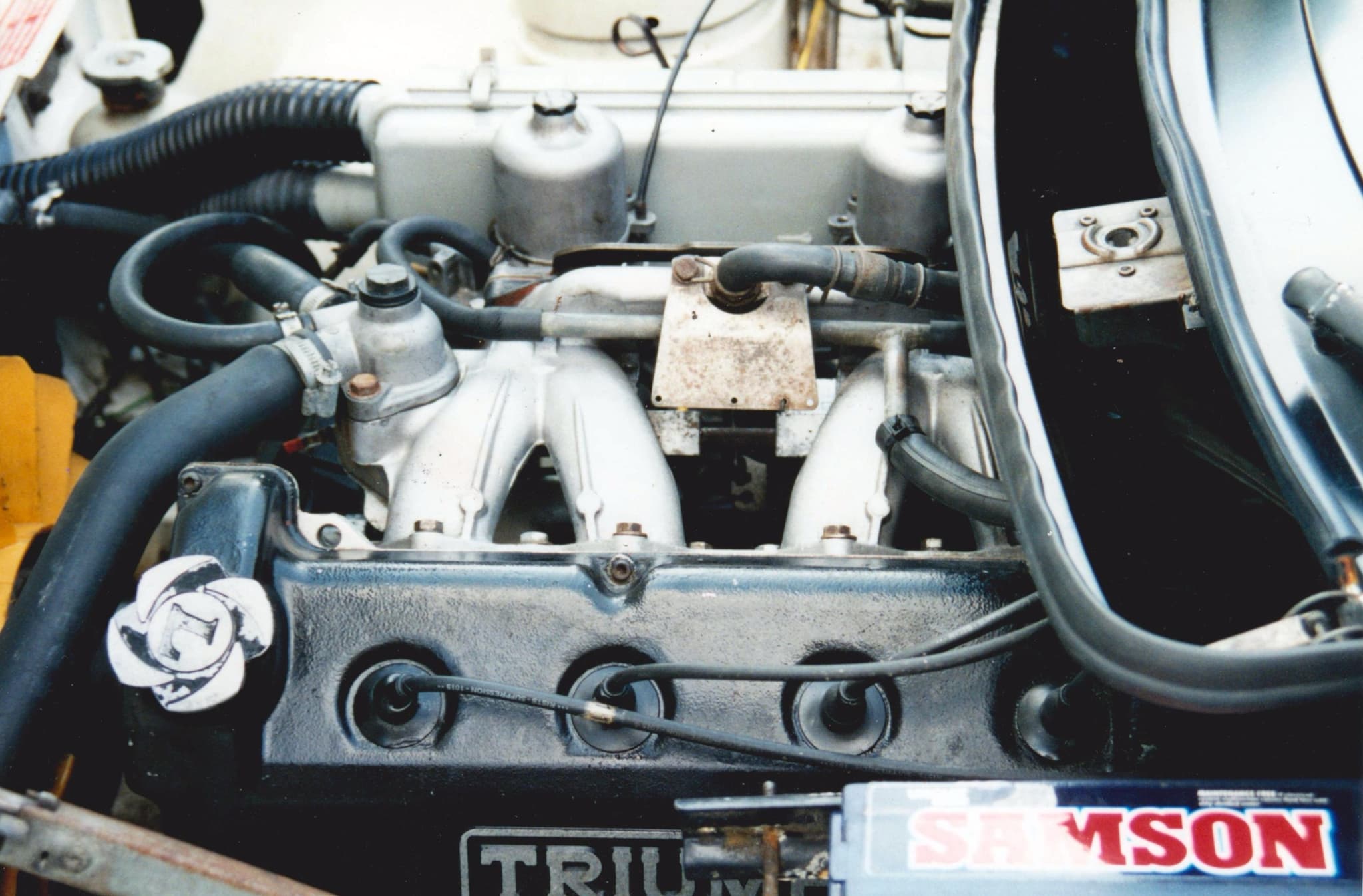 An engine bay seen from the left, with a sixteen-valve cylinder head and carburettors. Opens a larger view