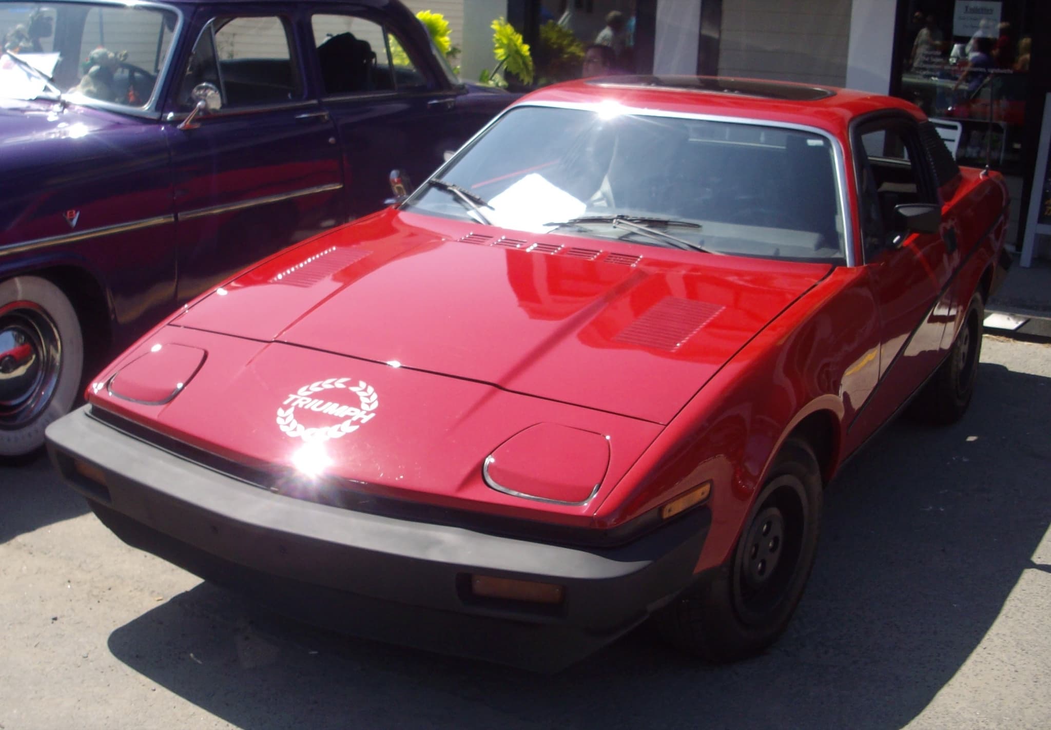 A red coupé with a laurel-wreath decal and long bumpers at an outdoor car show.