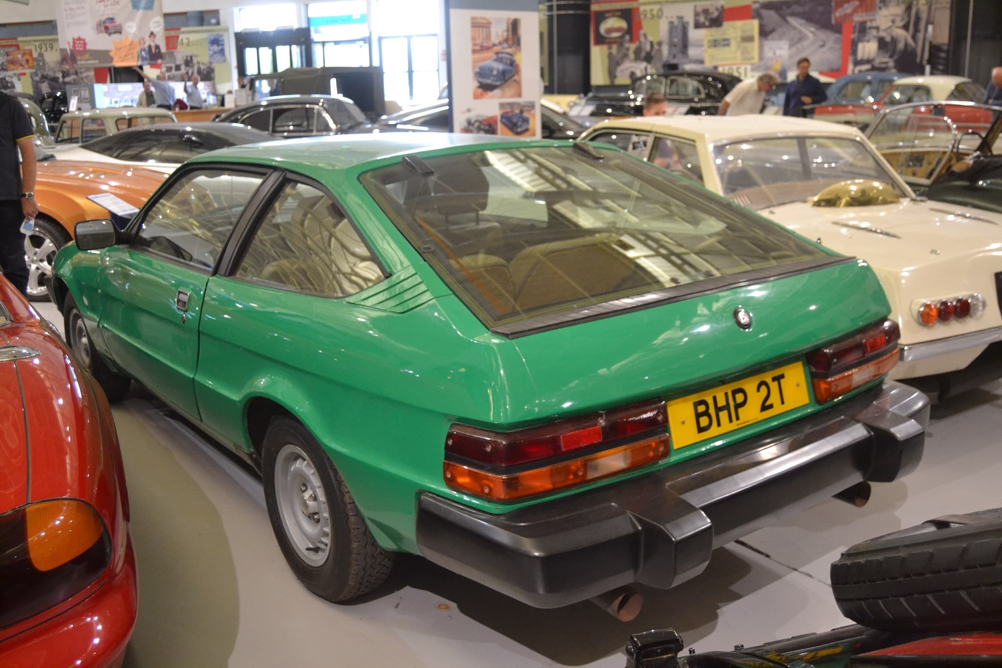 The rear of a green hatchback coupé with long side windows, in a museum.