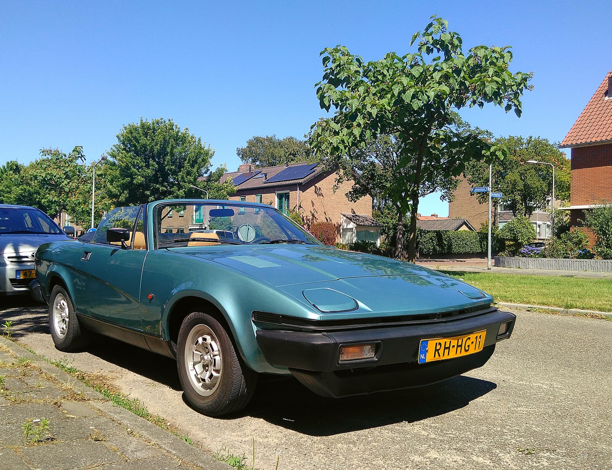 A metallic teal convertible with its hood down, parked on a sunny residential street.