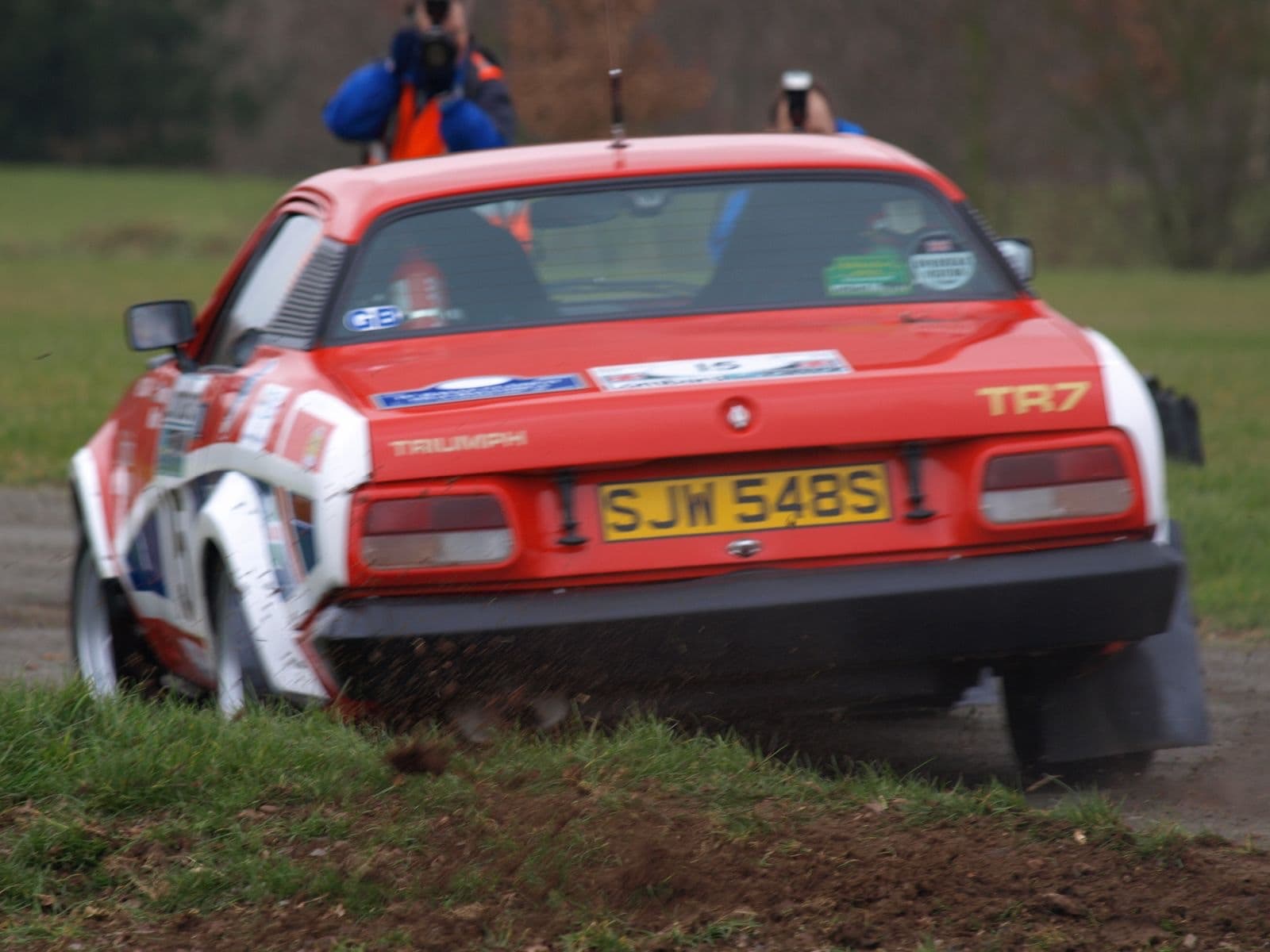 A red, white and blue rally car sliding away from the camera on a muddy stage.