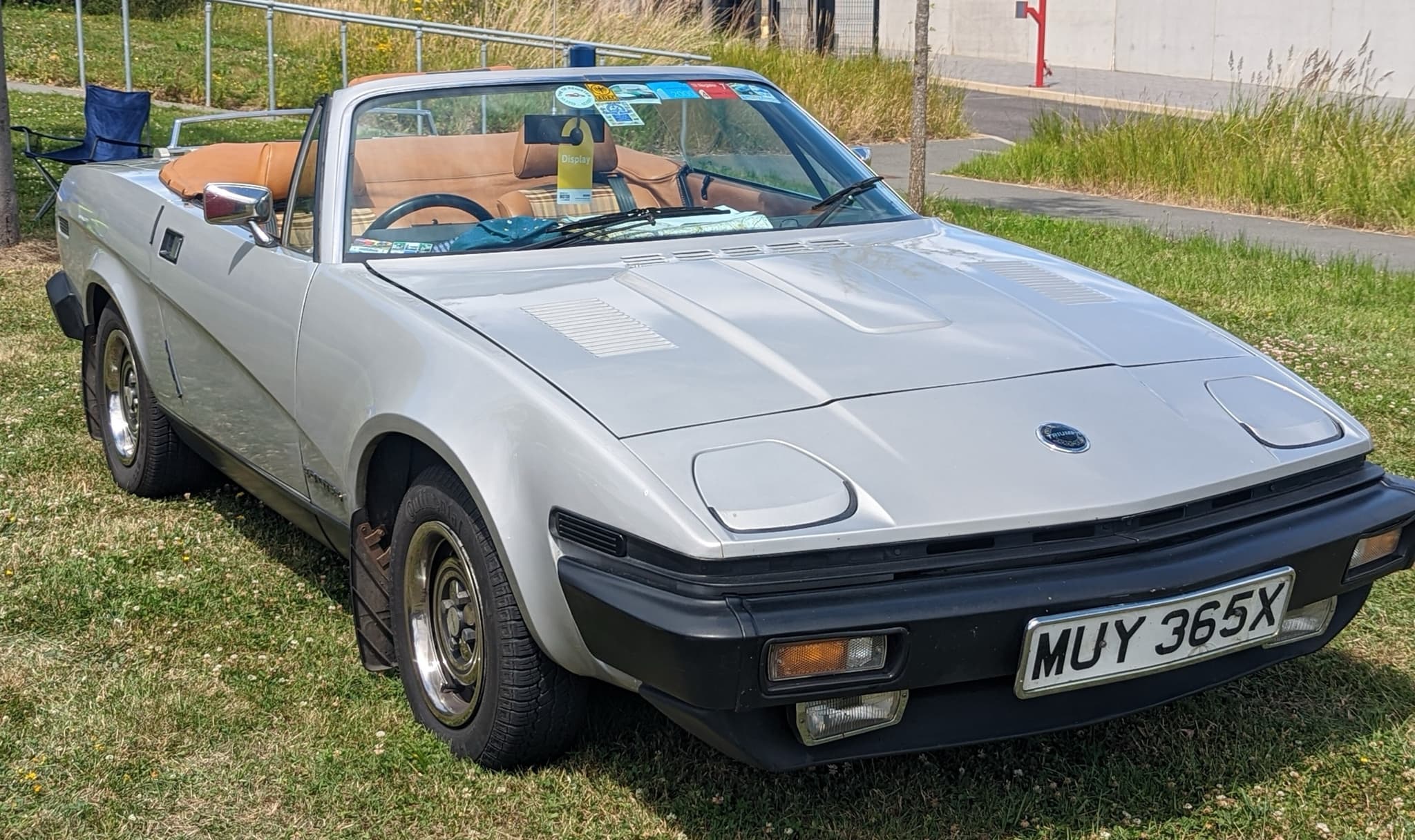 A silver convertible with its hood folded away, in a show car park. Opens a larger view