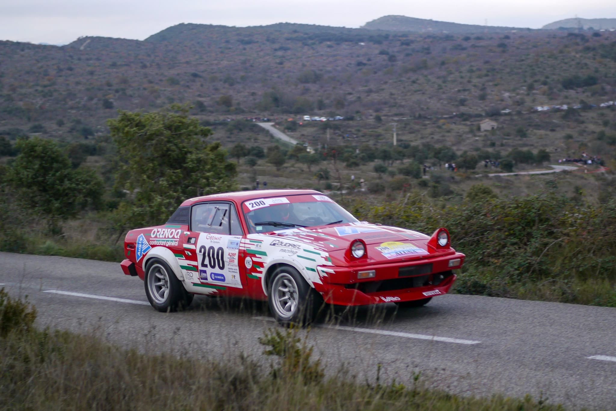 A white and red rally coupé numbered 200 on a hillside road.