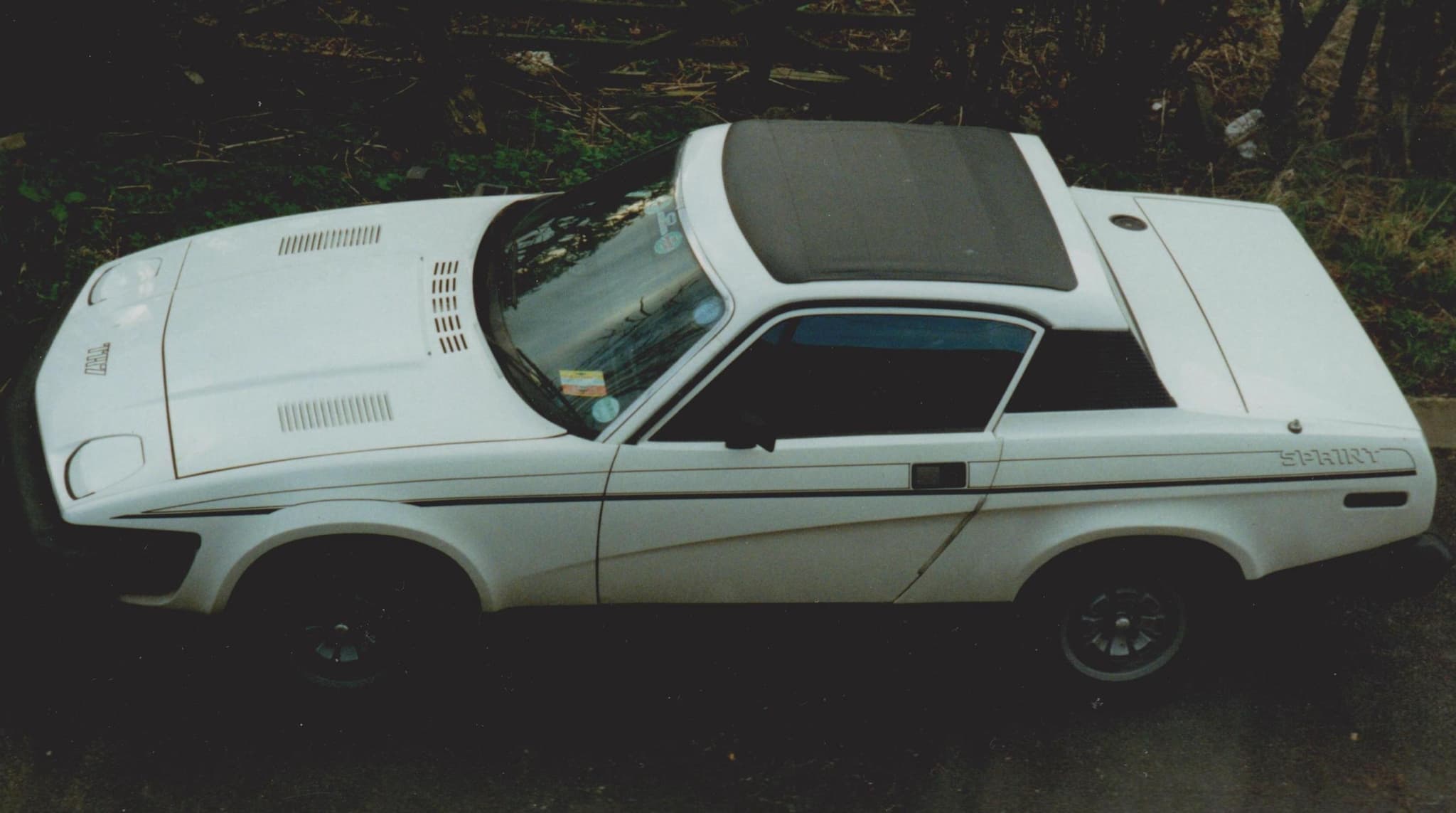 A white coupé side-on with a dark stripe along its flank. Opens a larger view