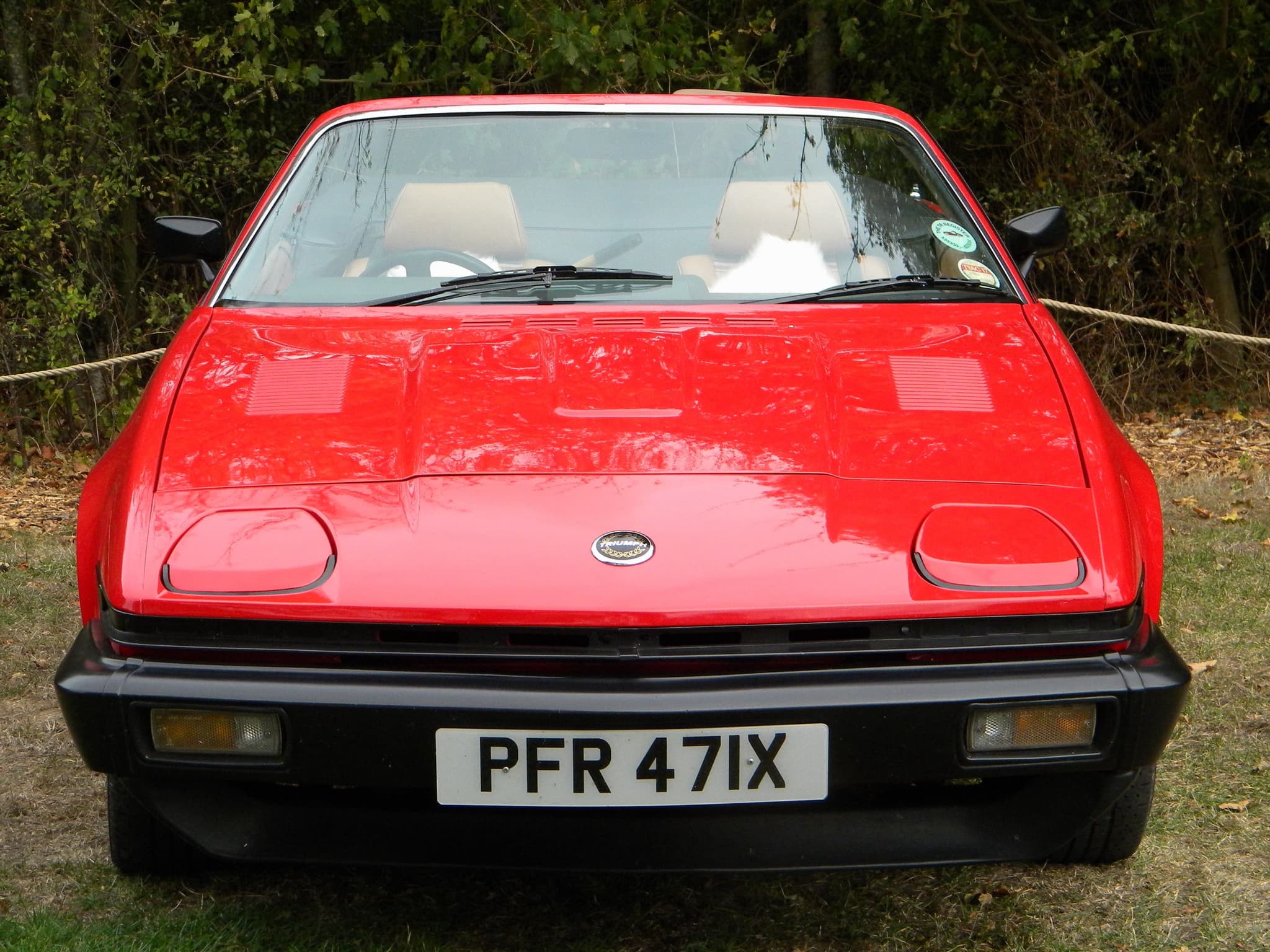 A red sports car seen head-on, showing a small round nose badge, two raised panels on the bonnet and a black bumper.