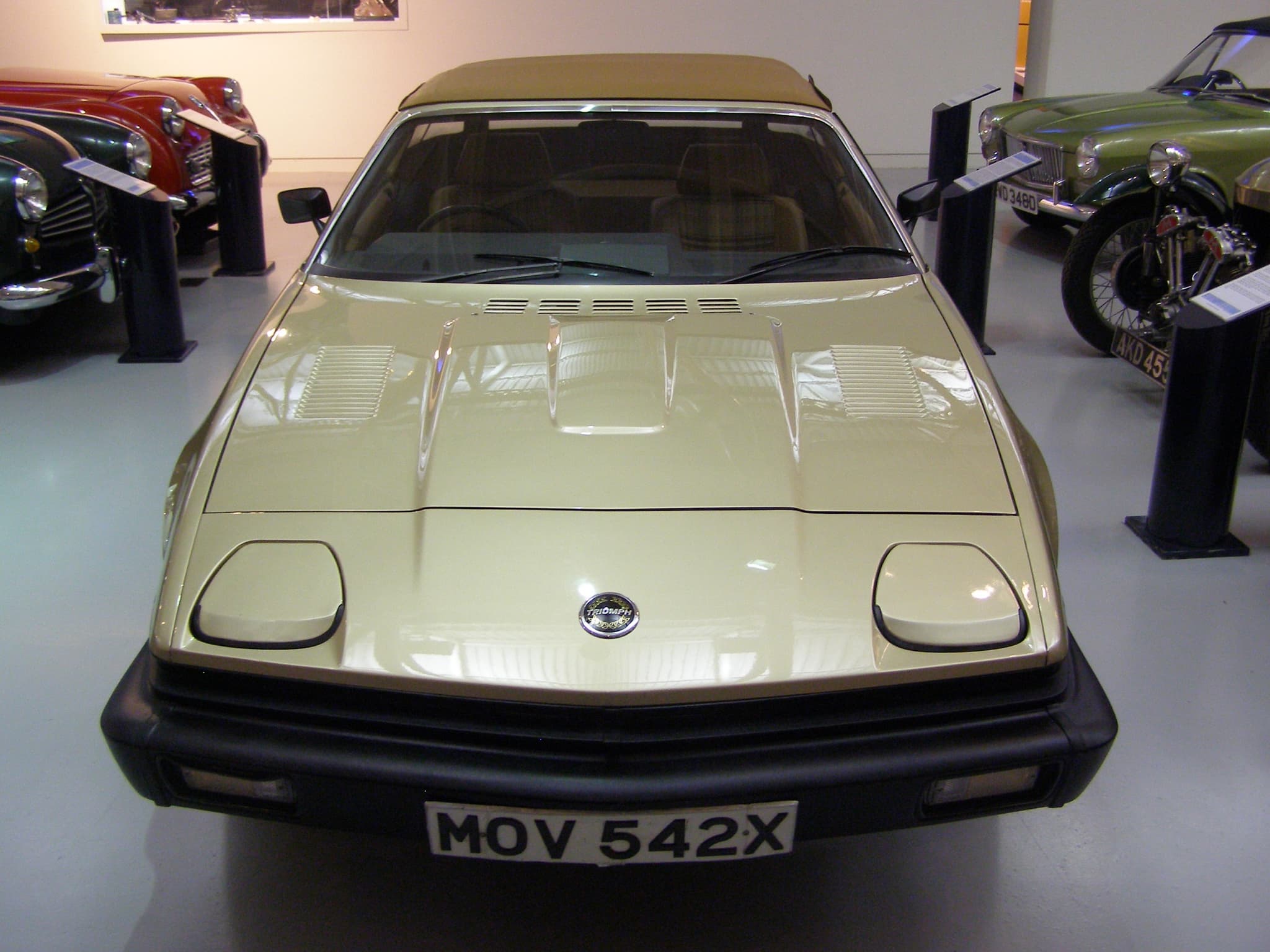 A champagne convertible with its hood up seen head-on in a museum.