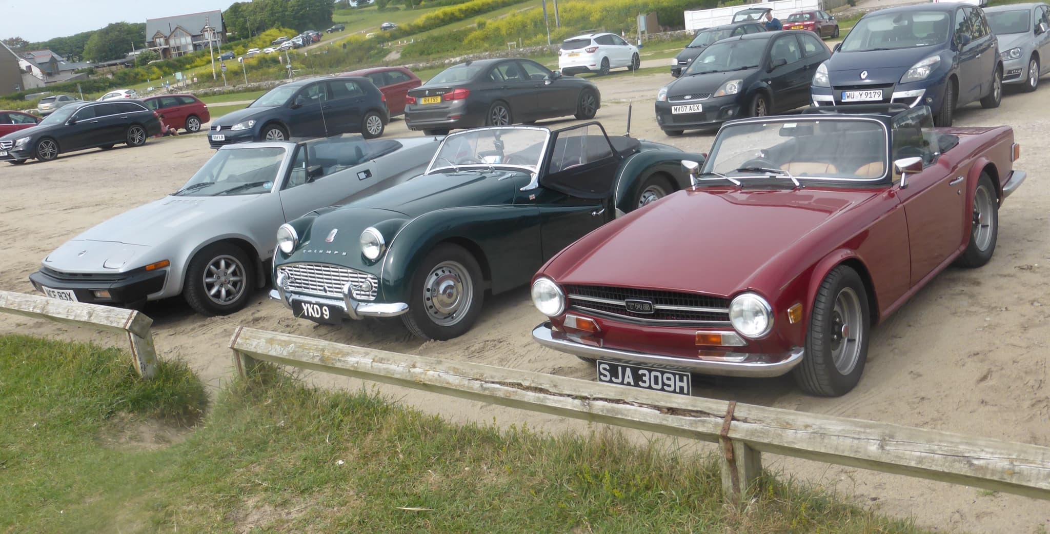 A silver wedge-shaped convertible parked in a row with a green round-fronted roadster and a red square-tailed roadster.