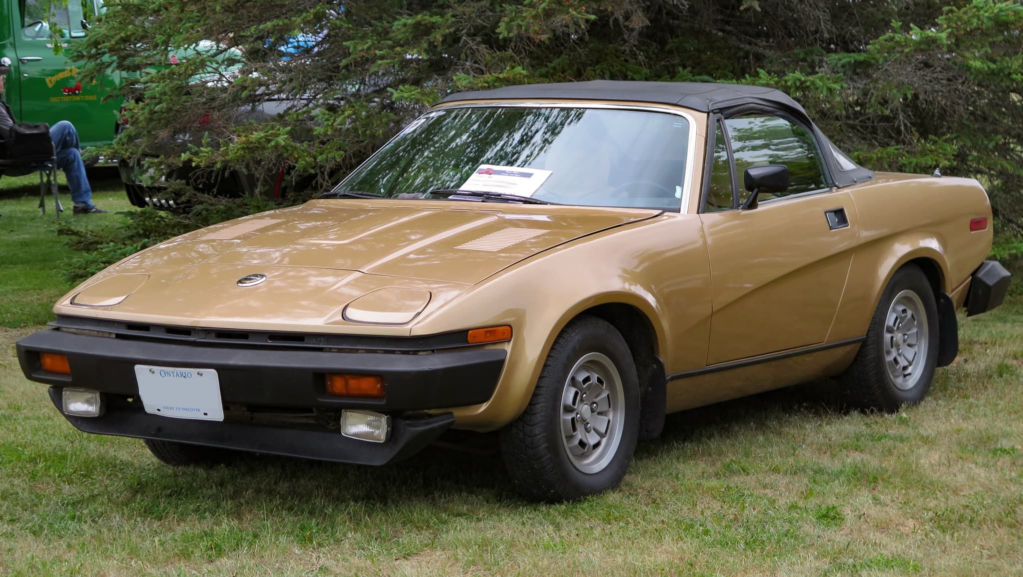 A gold convertible with its hood up, parked outdoors.