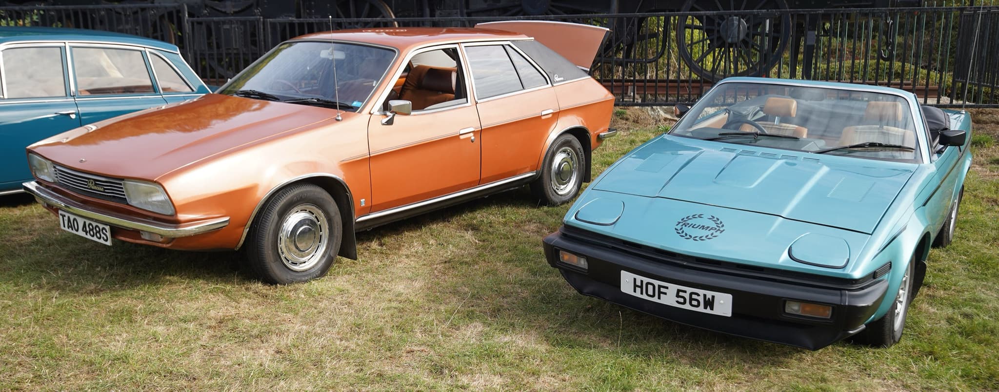 A light blue wedge-shaped convertible parked beside an orange wedge-shaped saloon on grass.