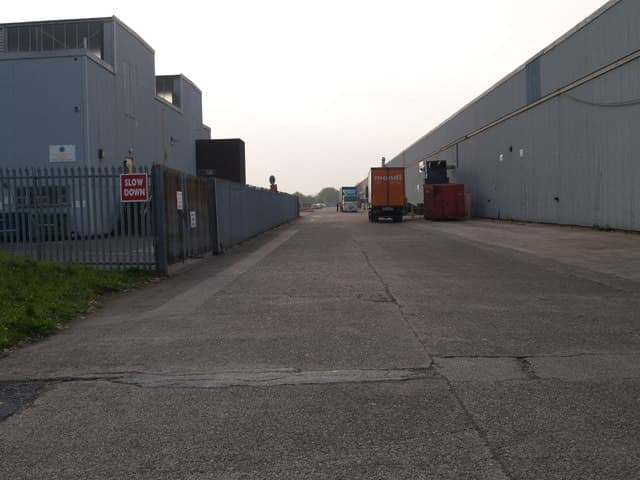 A road running between long grey factory units on a trading estate.