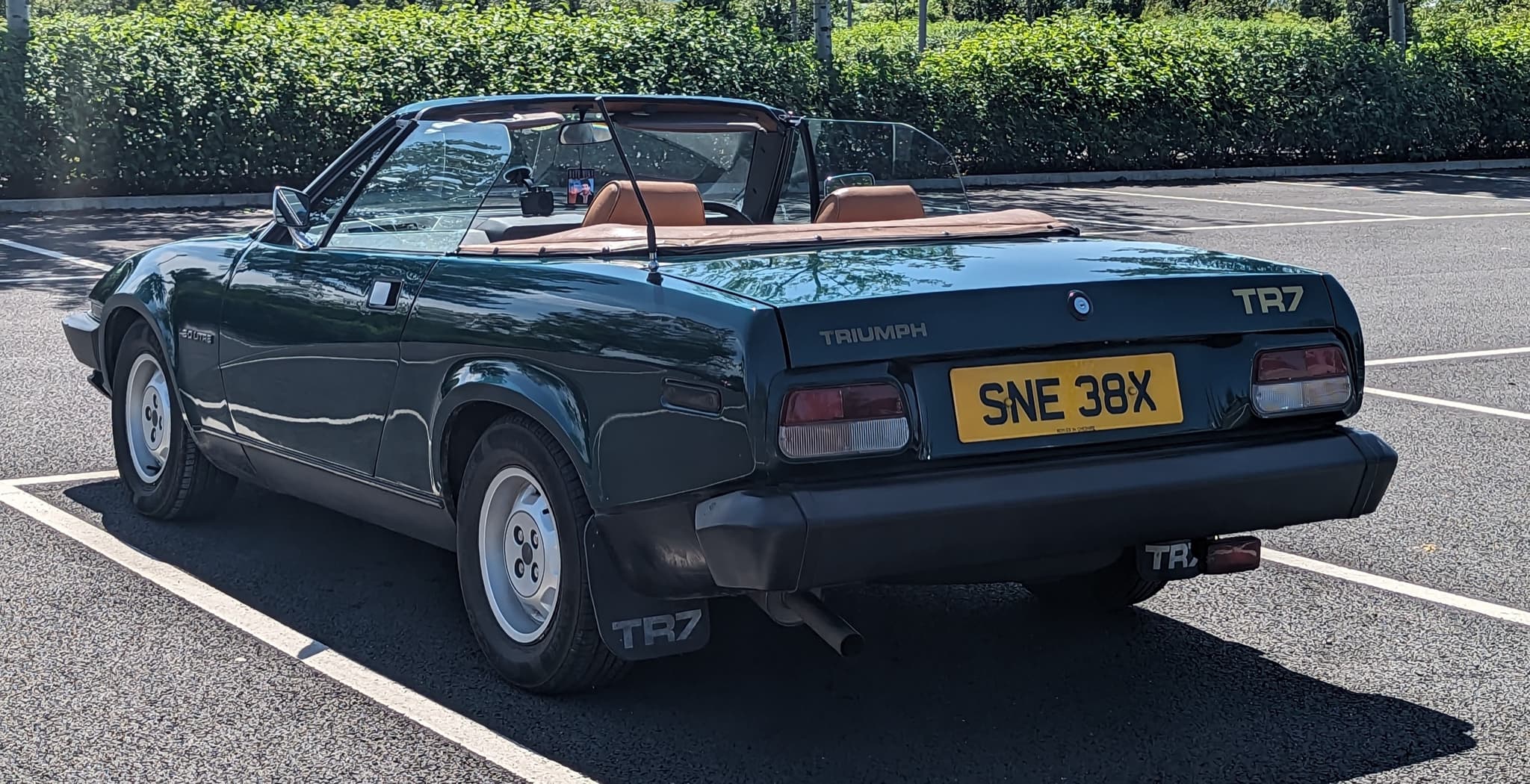 A dark green convertible from behind and to one side, showing the low rear deck and the folded hood.
