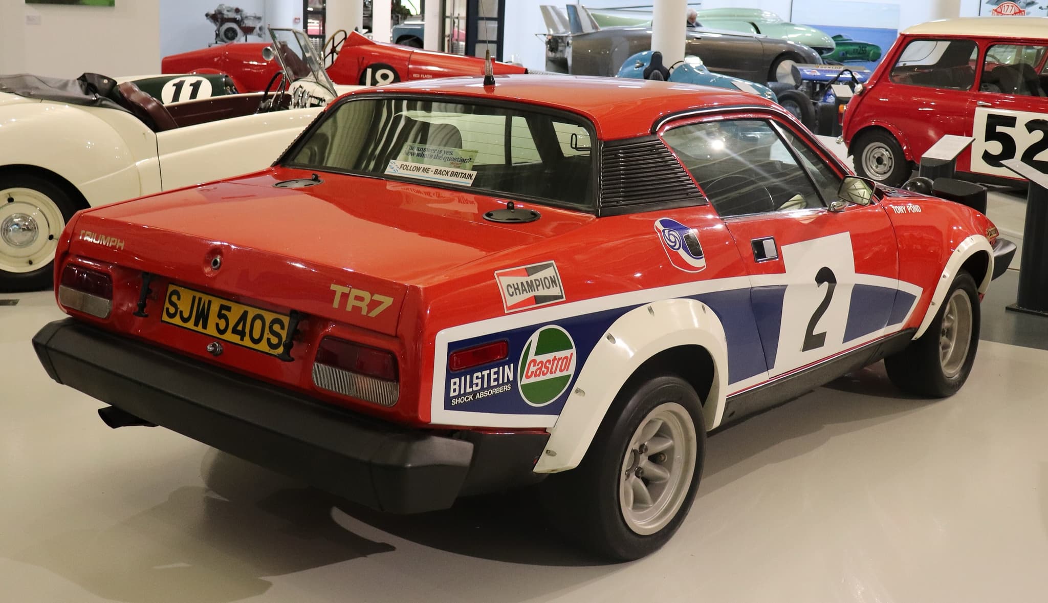 The tail of a red, white and blue rally car numbered 2, with sponsor decals, in a museum hall.