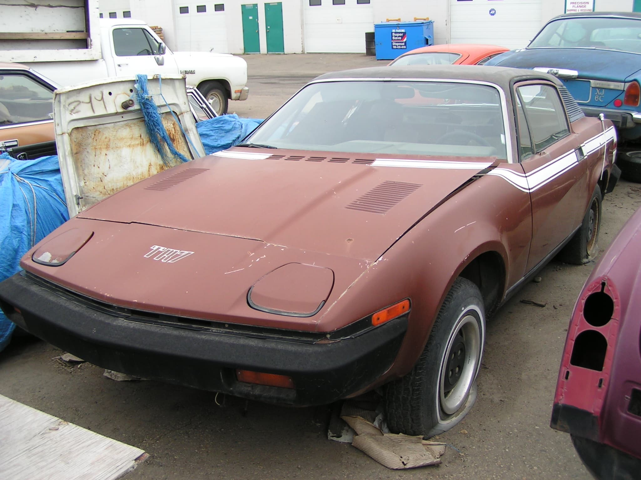 A faded brown early coupé standing neglected in a yard.