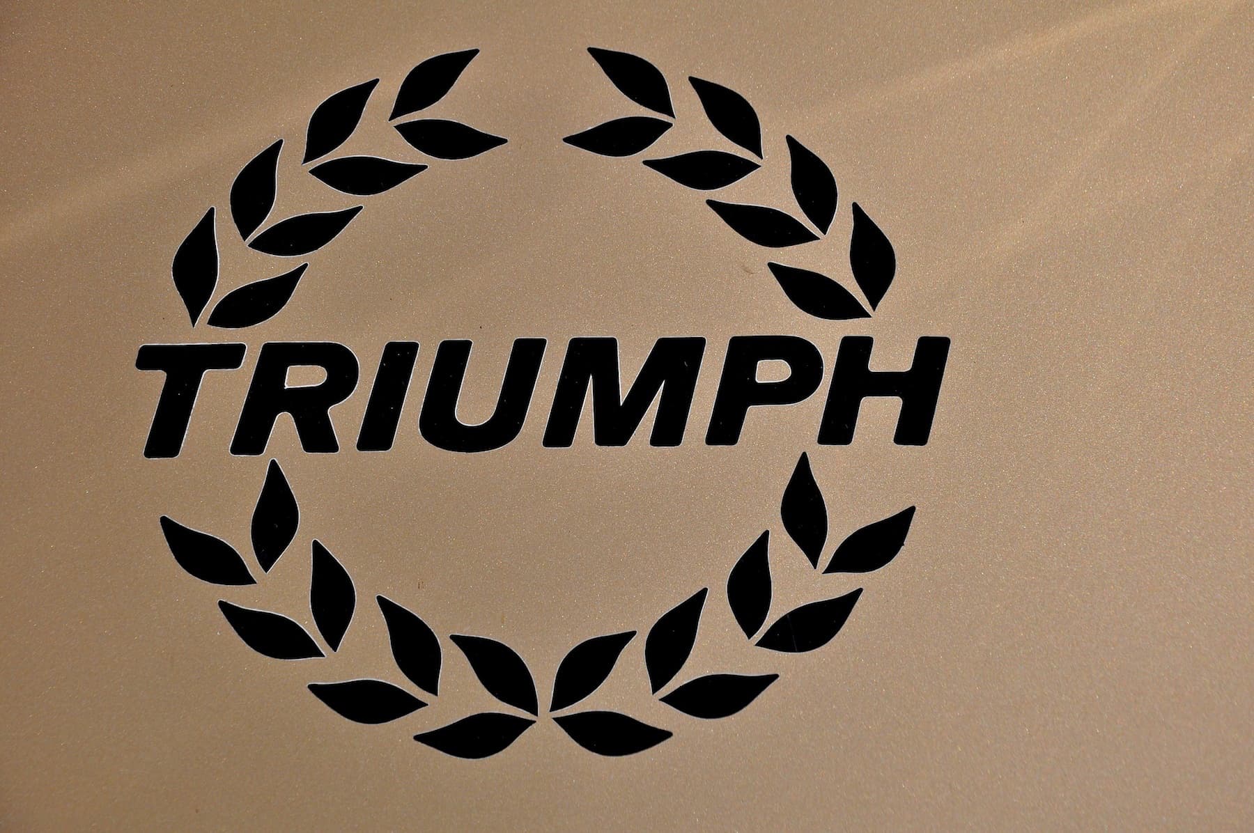 A close-up of a black laurel-wreath TRIUMPH decal on a pale gold bonnet.