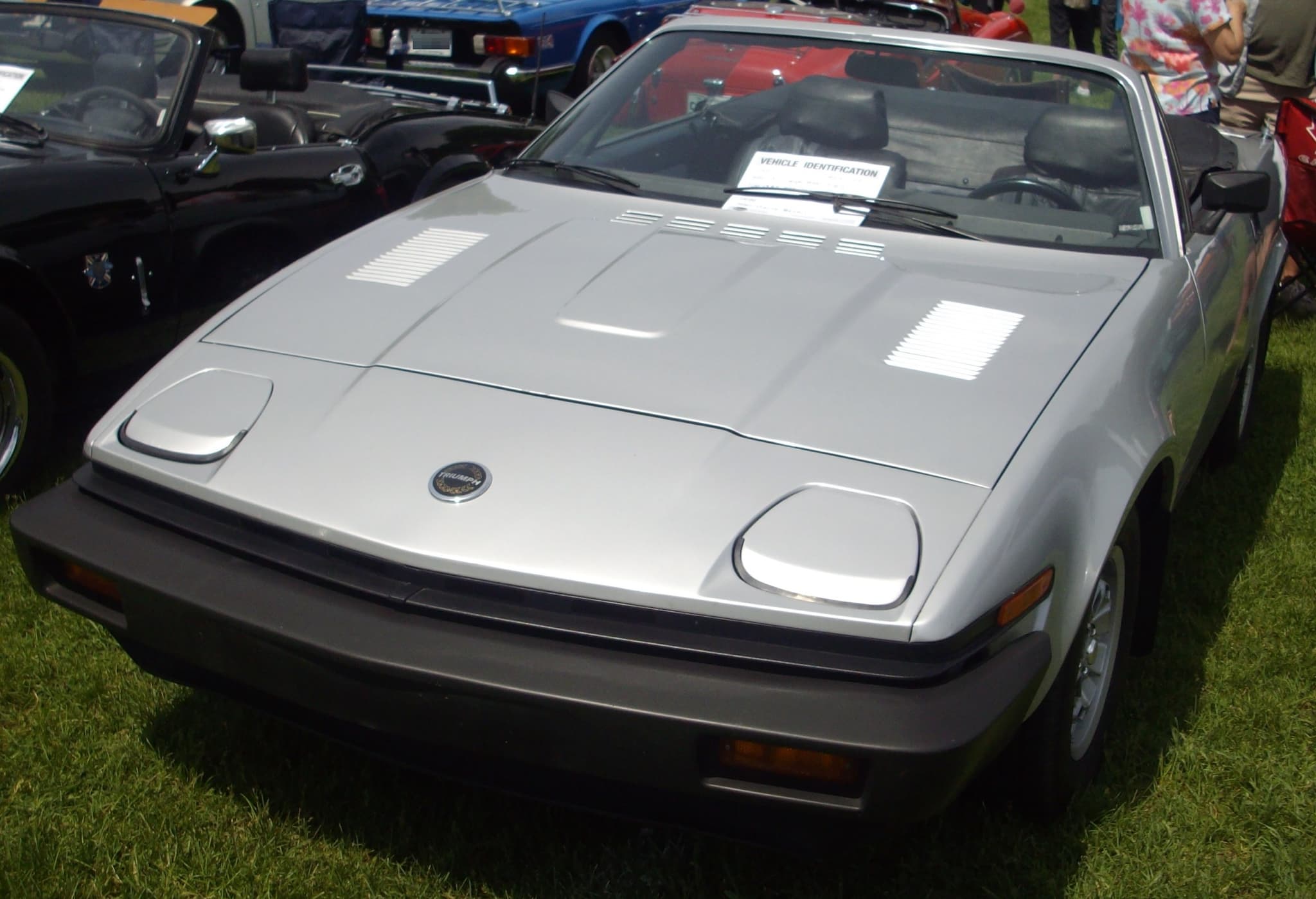 A silver convertible with its hood down and long bumpers at an outdoor car show.