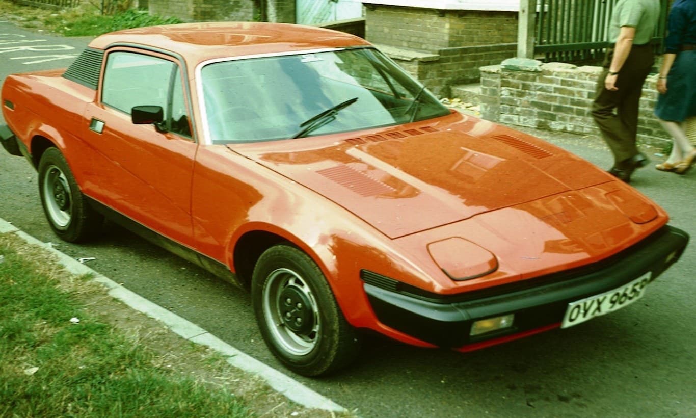 An orange wedge-shaped coupé parked at a kerb in a colour photograph from the 1970s.